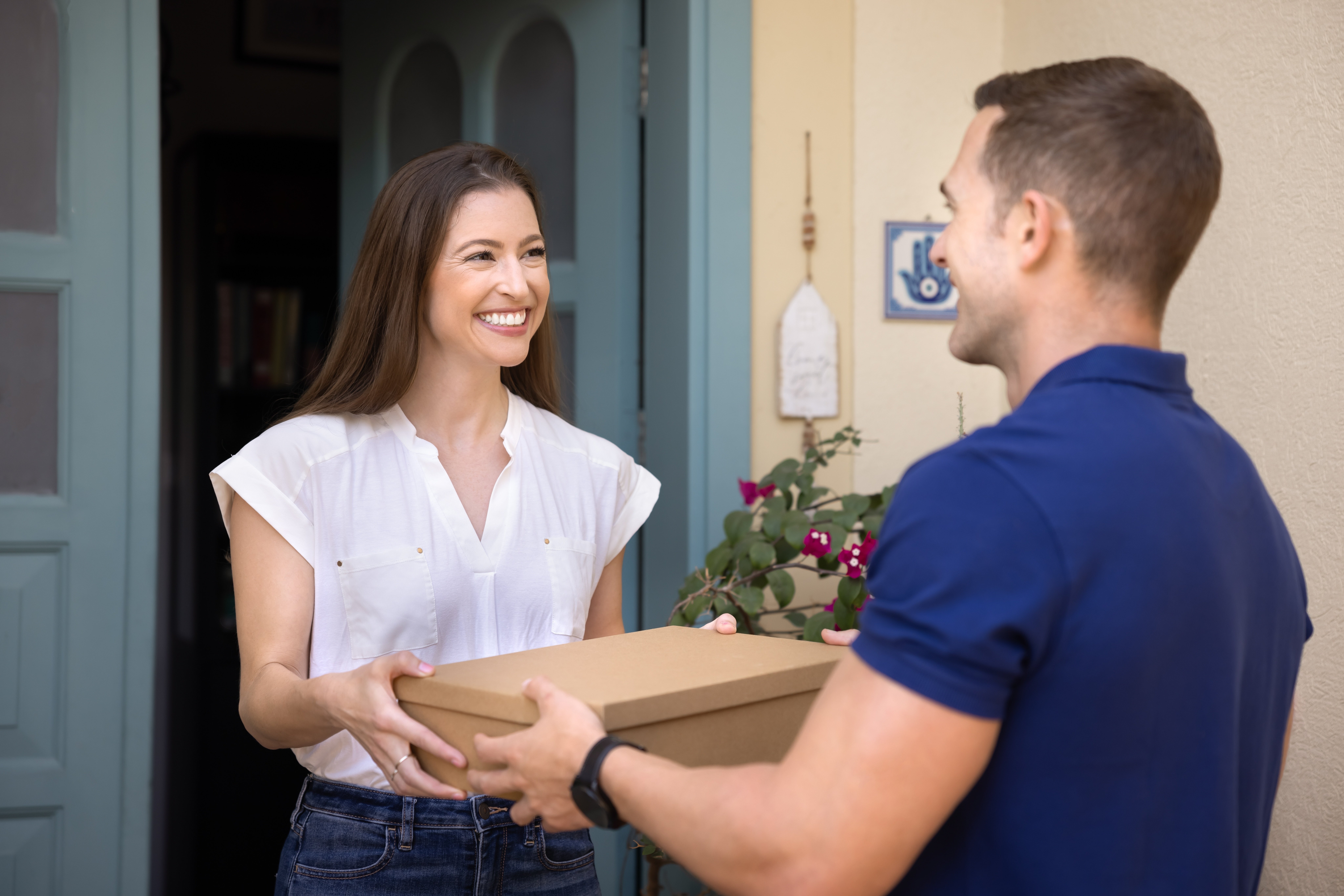 Mujer sonriendo, mientras un transportista le entrega su paquete. Un ejemplo de los beneficios de Carrier Hub de Pinit.