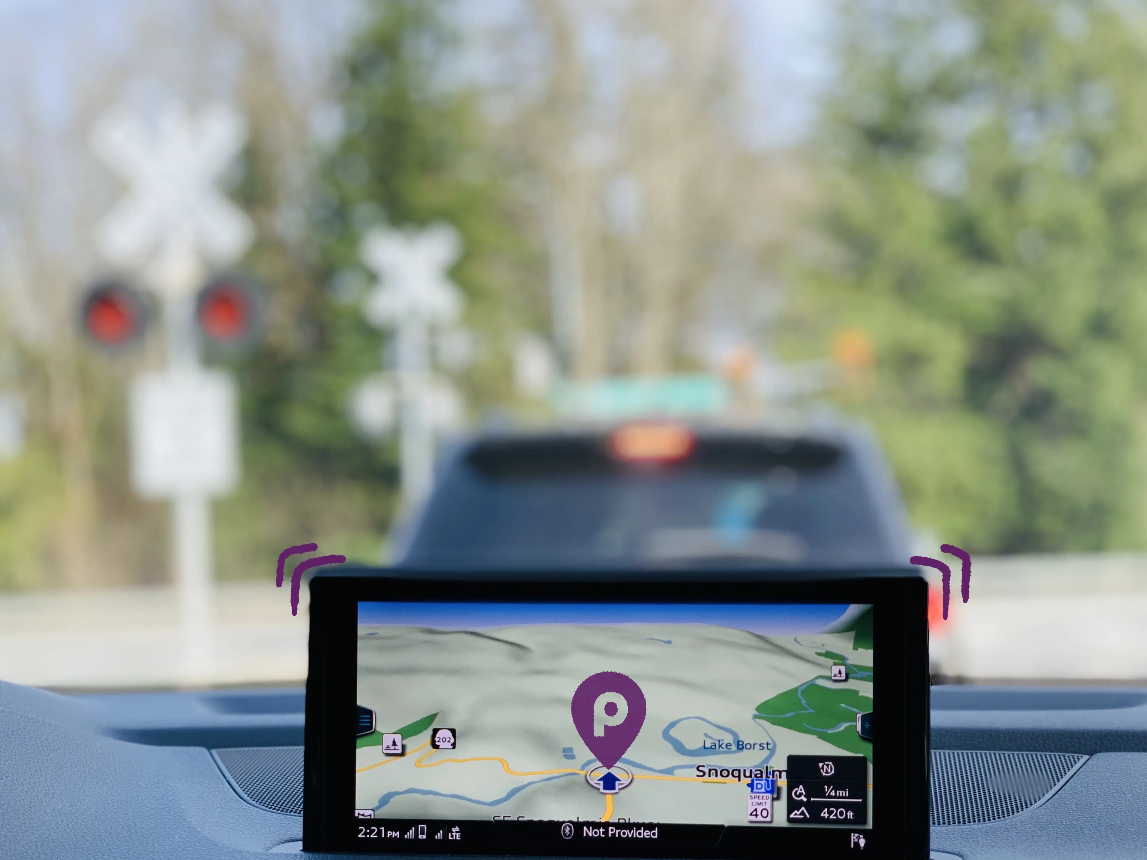 Pantalla de navegación GPS dentro de un vehículo, mostrando una ruta con señalización de cruce ferroviario al fondo.