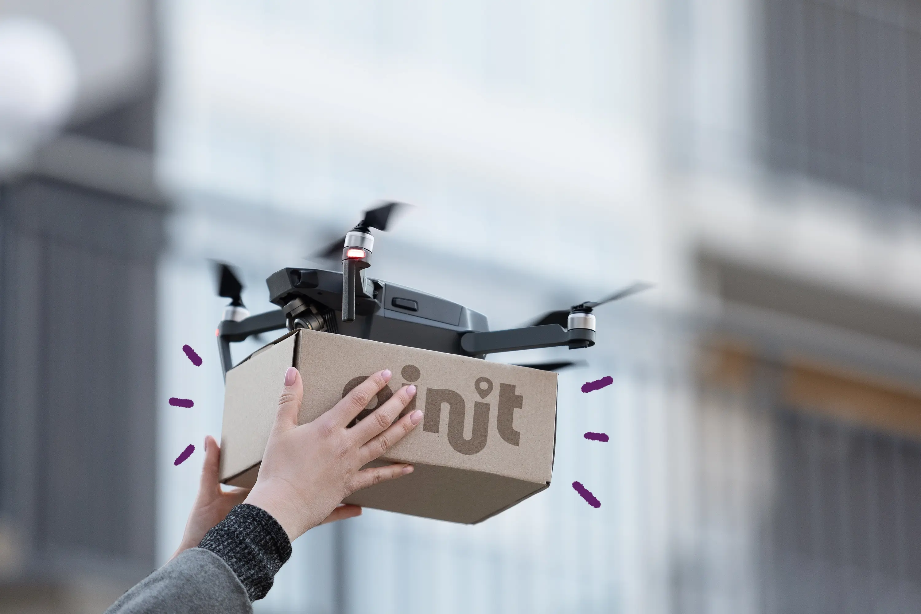 Dron realizando una entrega de última milla con un paquete marcado con la marca Pinit, sostenido por una persona.